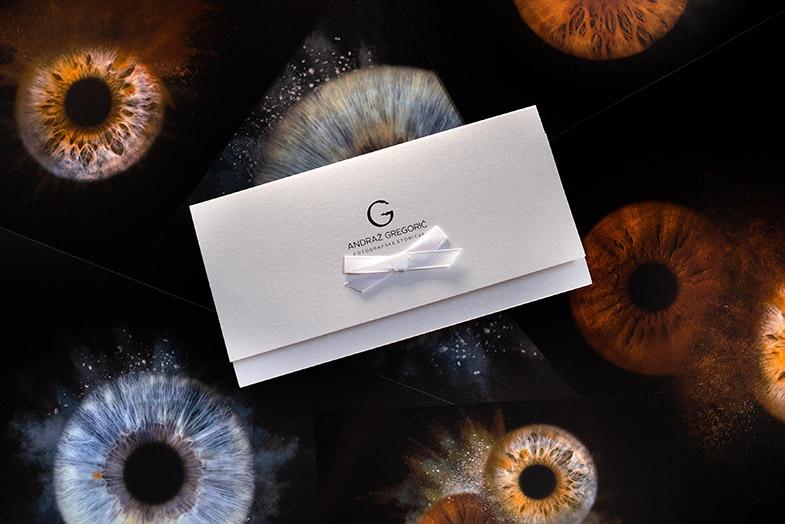 Darilni bon za fotografiranje oči – elegantna kuverta z belo pentljo na ozadju makro fotografij šarenic